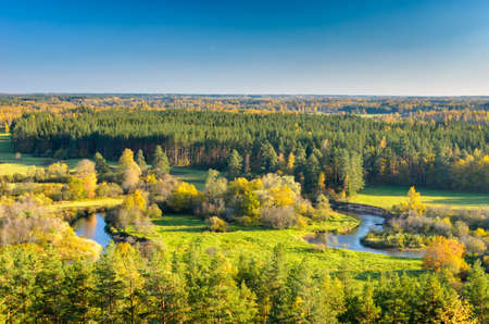 A bright natural landscape in the fall season. A view over the forest, meadows and the river in...