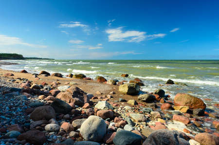 Sunny day with blue sky on the beach with many stones. Waves on the background.の写真素材