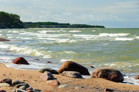 Steep bank on the Baltic sea coastline. Stones on the beach. Sunny day in summer. Waves in the background.の写真素材