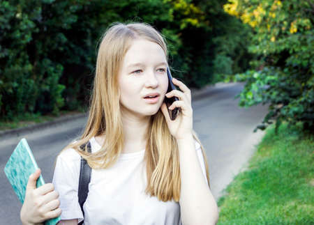 A young girl is talking on the phone. A teenager with a surprised face stands against the background of trees.の写真素材
