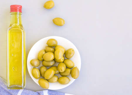 A glass bottle of olive oil, a bowl of olives, and a towel. Grey background, space for textの写真素材
