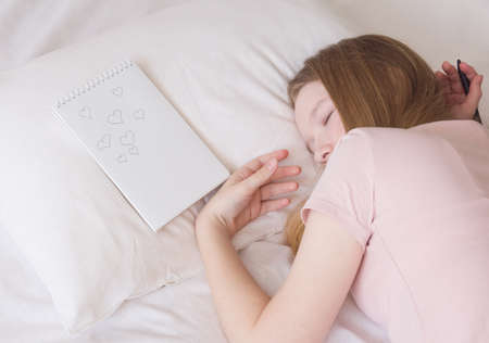 A girl with long blond hair fell asleep on the bed, a Notepad next to her, a pen in her hands....