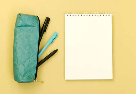 Top view of a Desk with a pencil case and an empty Notepad on a yellow background. Flat lay of items...