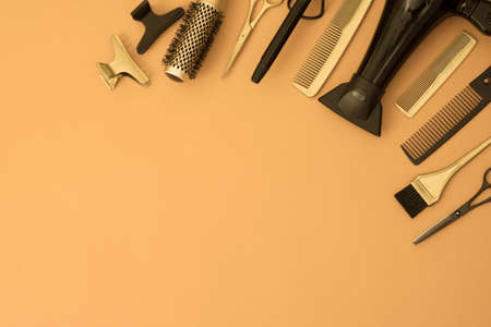 Banner with hairdressing tools. Gold and black hair salon accessories in the corner on an orange and yellow background with space for text. Hair dryer, comb, scissors, brush and hair clips.の写真素材