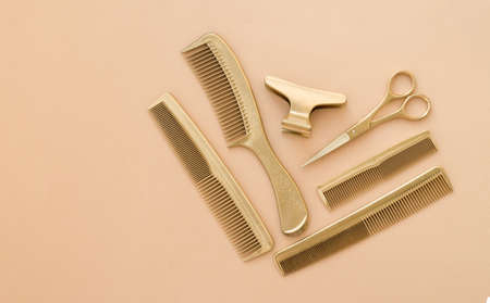 Gold hairdressing tools on a beige background. Template with hair salon accessories and space for...