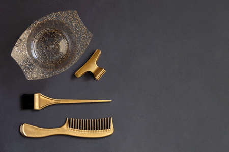 Golden hairdressing tools for hair coloring on a dark gray background with copy space. On the table...