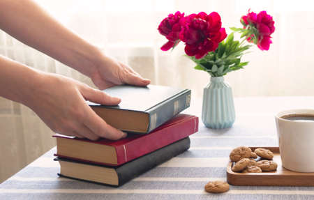 Reading a book at a table by the window. Book in hand, morning coffee at home or in a cafe, cozy...