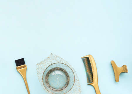 Hairdressing tools in gold color on a blue background. Hair salon accessories for coloring, bowl,...
