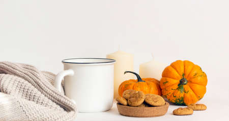 Morning coffee, autumn atmosphere. Mug, scarf, cookies, pumpkins and candles on a white tableの写真素材