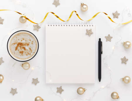 White sheet of notebook with pen on white table with cup of cocoa or coffee, stars, Christmas balls...