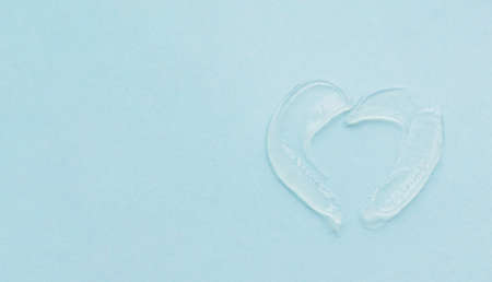 The texture of the swatch lip balm in the shape of heart. Transparent ointment on blue background and copy spaceの写真素材