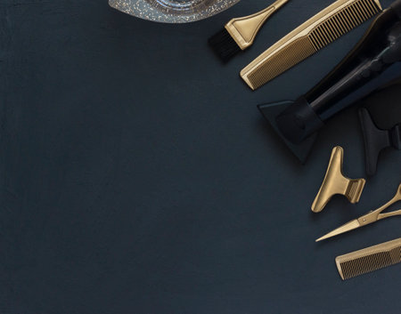 Hairdressing tools in black and gold on gray concrete background. Hair salon accessories, hair dryer, combs, scissors and hair clips in the corner and copy spaceの写真素材