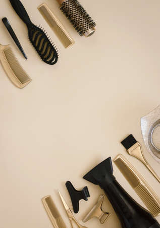 Banner with hairdressing tools. Gold and black hair salon accessories in the corner on a light beige background with space for text. Hair dryer, comb, scissors, brush and bowl, hair clips.の写真素材