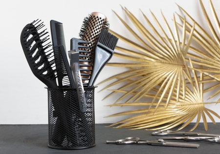 Hairdressing tools in stand near golden palm leaves on gray background. Template with hair salon accessories.の写真素材