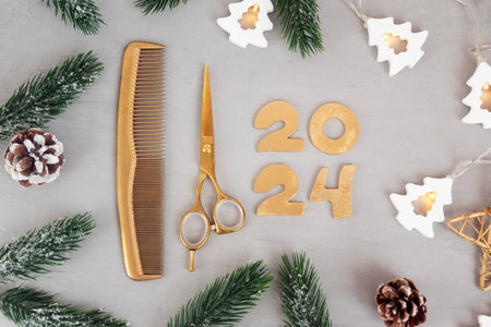 Numbers 2024 golden colored scissors and comb with fir twigs on gray background. Template greeting card of hairdresser or hair salon.の写真素材