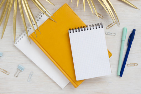 Different notebooks pens paper clips stationery on table top view. Summer concept with palm leaves mocap for letteringの写真素材