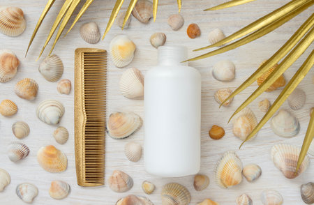 White plastic bottle without inscription hair comb summer background with seashells and golden palm...
