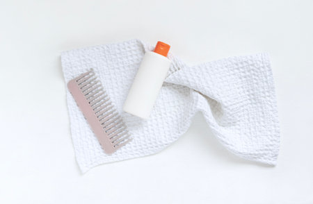 Plastic white shampoo bottle and comb on white textured towel. Idea of image of hair care product....