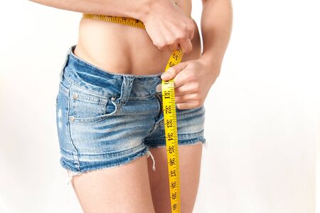 Model wearing blue jeans shorts measuring her waste with a yellow tapeの写真素材
