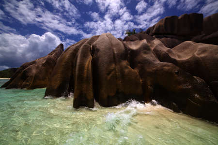 Blue sky laced with fluffy white clouds over a beautiful shore lined with smooth weather worn bouldersの写真素材