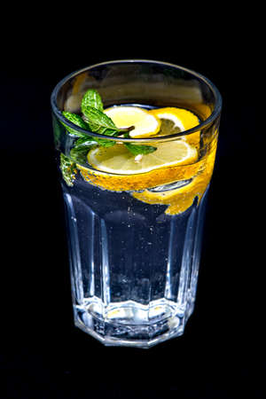 Glass Water with mint and yellow citron half isolated with a black background