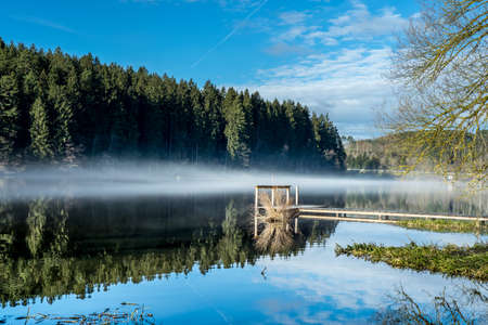Footbridge with fog and sunbeams and reflection in the water in the bavarian forestの写真素材