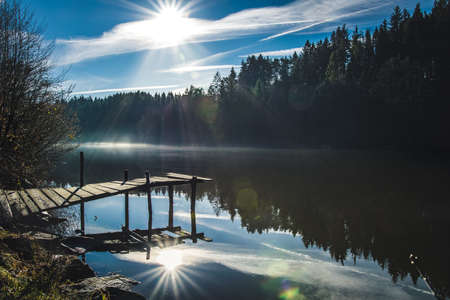 Footbridge with fog and Sunbeams and reflection in the water in the bavarian forestの写真素材