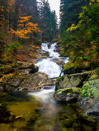 Big Waterfall with a small creek in the autumn with orange leaf and wet stones with moss on the rocks in the bavarian forestの写真素材