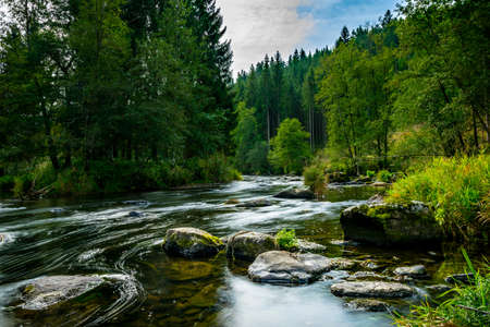 River with stones in the water and reflection on the creek and clouds on the sky in the bavarian forestの写真素材