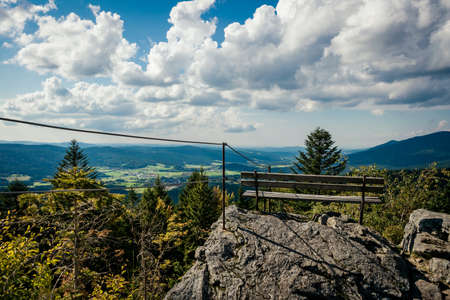 Bench on top of a mountain on the rock with clouds on the sky and a view in the valley in the bavarian forestの写真素材