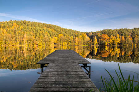 Footbridge on a lake in the autumn with orange and yellow trees and reflection from the forest on the water in the bavarian forestの写真素材