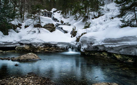 Frozen creek in the winter with reflection on the water and snow on the stones and rocks in the bavarian forestの写真素材