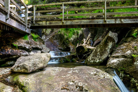 Bridge with a waterfall in the green nature in the bavarian forest with rocks and stones in front ofの写真素材
