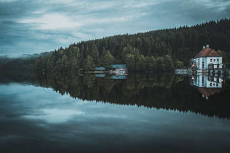 Reflection from houses and trees on the lake with fog and dusk in the backgroundの写真素材