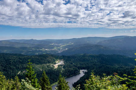 View from a top of a mountain in the valley with a lake and clouds on the sky in the bavarian forestの写真素材