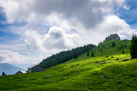 On the top of a mountain in austria with a alm and grass and clouds on the sky and sunrays on the groundの写真素材