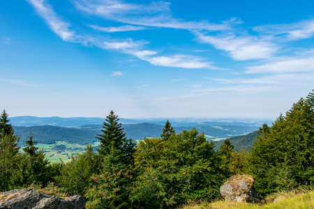 View from top of a mountain in the valley with clouds on the sky and mountains on the background and stones and trees in front of in the bavarian forestの写真素材