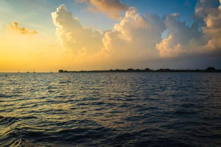 Sunset in the Maldives with reflection of the Sun in the water and blue and orange colored clouds in the skyの写真素材