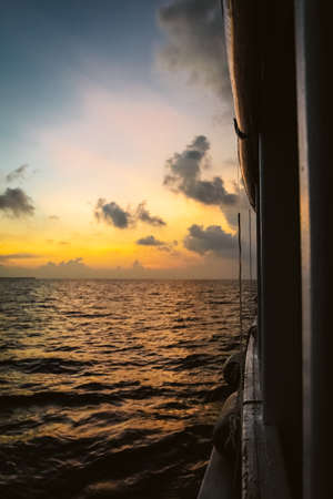 Sunset in the Maldives with reflection of the Sun in the water and blue and orange colored clouds in the skyの写真素材