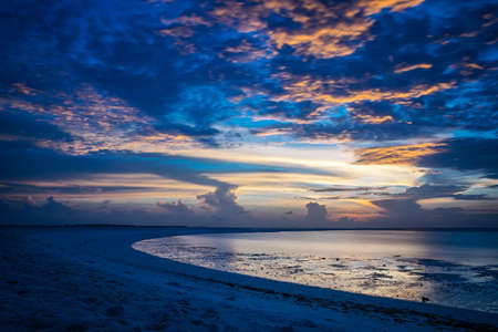 Sunset in the Maldives with reflection of the Sun in the water and blue and orange colored clouds in the skyの写真素材