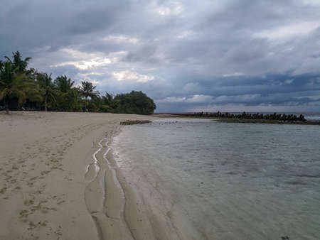Maldives with turquoise clear water and many palm trees and clouds in the skyの写真素材