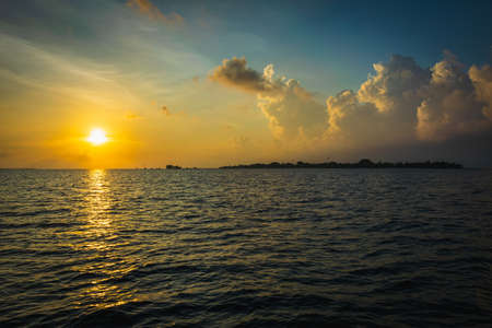 Sunset in the Maldives with reflection of the Sun in the water and blue and orange colored clouds in the skyの写真素材