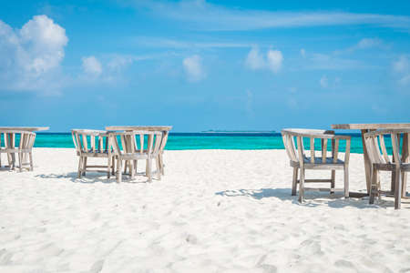 Chairs and Tables on the white beach at the maldives with the turqoise ocean in the background and clouds on the blue skyの写真素材