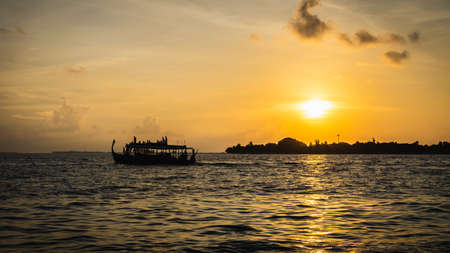 Sunset in the Maldives with reflection of the Sun in the water and blue and orange colored clouds in the skyの写真素材
