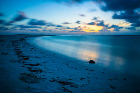 Sunset in the Maldives with reflection of the Sun in the water and blue and orange colored clouds in the skyの写真素材
