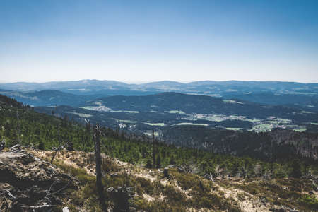 View from the top of a mountain into the valley with clouds in the blue sky and beautiful green trees and lots of rocksの写真素材