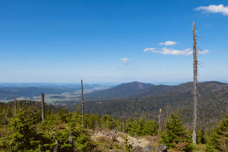 View from the top of a mountain into the valley with clouds in the blue sky and beautiful green trees and lots of rocksの写真素材
