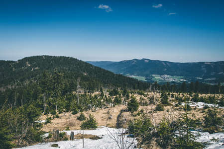 View from the top of a mountain into the valley with clouds in the blue sky and beautiful green trees and lots of rocksの写真素材