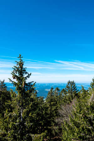 View from the top of a mountain into the valley with clouds in the blue sky and beautiful green trees and lots of rocksの写真素材
