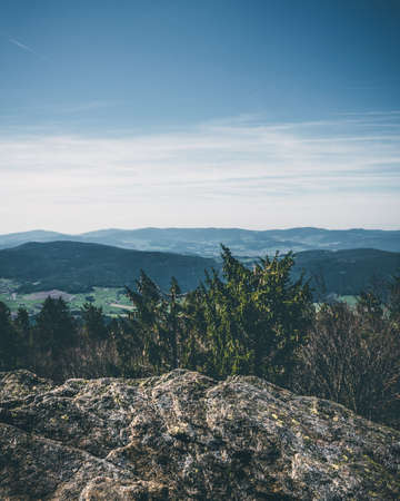 View from the top of a mountain into the valley with clouds in the blue sky and beautiful green trees and lots of rocksの写真素材